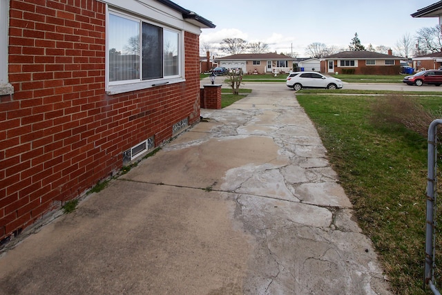 view of home's exterior featuring a residential view, concrete driveway, a lawn, and brick siding