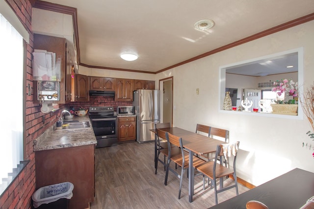 kitchen featuring dark wood finished floors, appliances with stainless steel finishes, under cabinet range hood, ornamental molding, and a sink