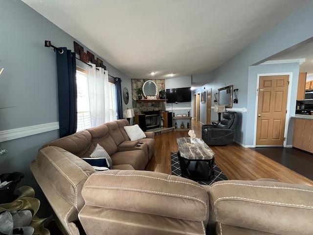 living area featuring baseboards, wood finished floors, and a stone fireplace