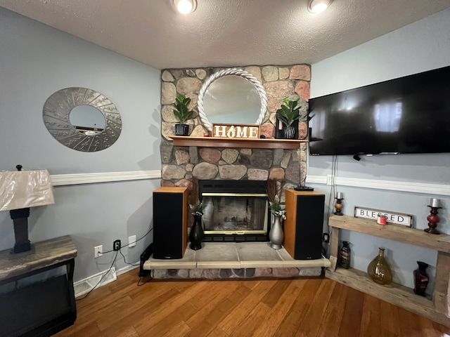 living area featuring a textured ceiling, baseboards, wood finished floors, and a stone fireplace