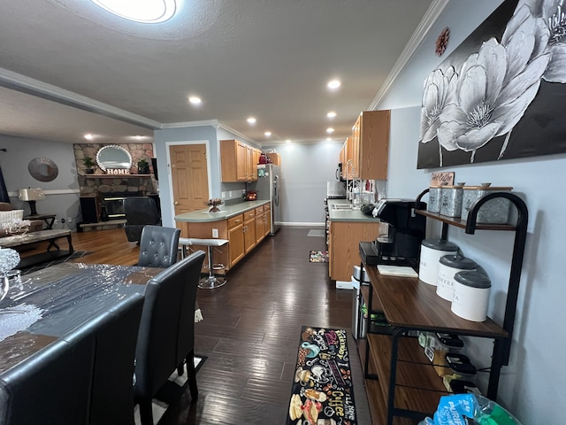 kitchen featuring dark wood finished floors, appliances with stainless steel finishes, ornamental molding, a stone fireplace, and recessed lighting