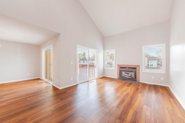 unfurnished living room with baseboards, wood finished floors, a fireplace with flush hearth, and a healthy amount of sunlight