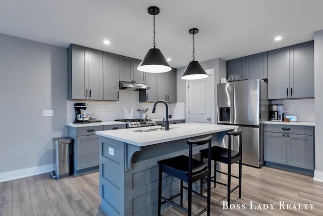 kitchen featuring light wood finished floors, gray cabinets, under cabinet range hood, stainless steel refrigerator with ice dispenser, and a sink