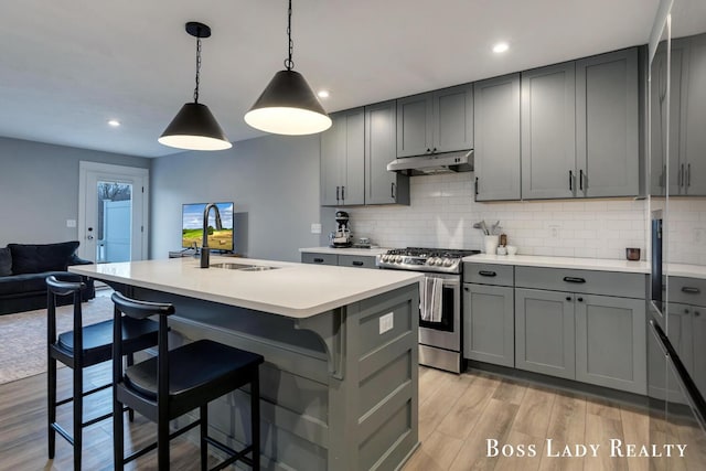 kitchen featuring under cabinet range hood, a sink, light countertops, gray cabinets, and stainless steel range with gas stovetop