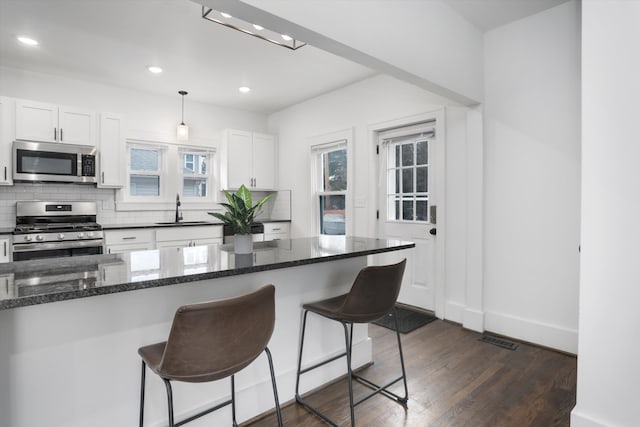 kitchen featuring appliances with stainless steel finishes, dark wood-style flooring, a sink, a kitchen bar, and backsplash