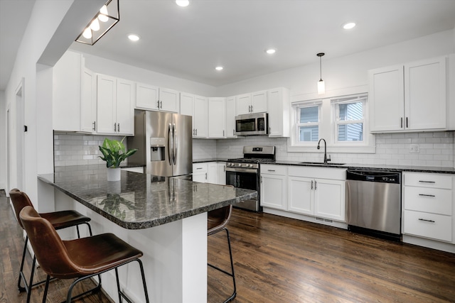 kitchen featuring dark wood-style flooring, a peninsula, stainless steel appliances, a kitchen bar, and a sink