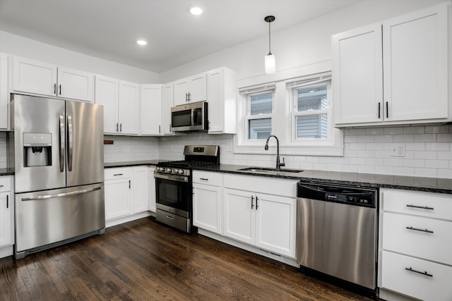 kitchen with tasteful backsplash, dark wood finished floors, appliances with stainless steel finishes, dark stone countertops, and a sink