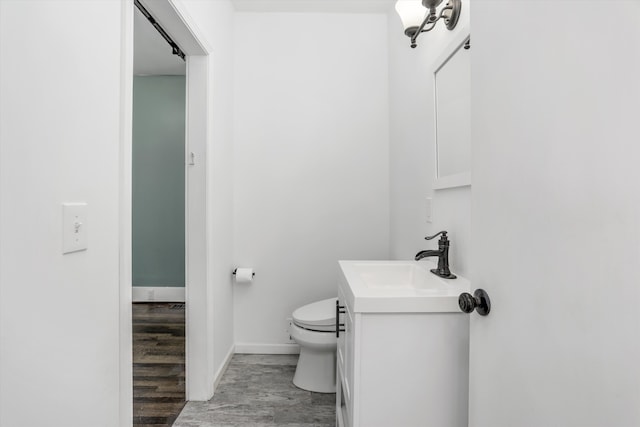 half bath featuring toilet, baseboards, wood finished floors, and vanity