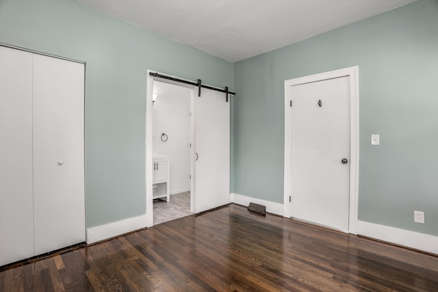 unfurnished bedroom with a barn door, baseboards, wood finished floors, ensuite bathroom, and a closet