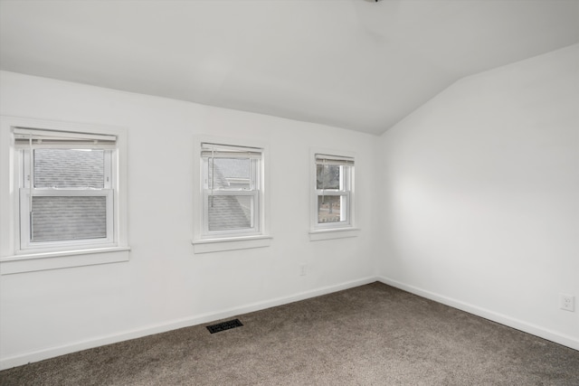 carpeted spare room featuring vaulted ceiling, visible vents, and baseboards