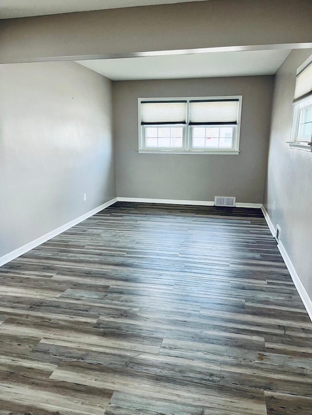 empty room featuring baseboards, plenty of natural light, visible vents, and wood finished floors