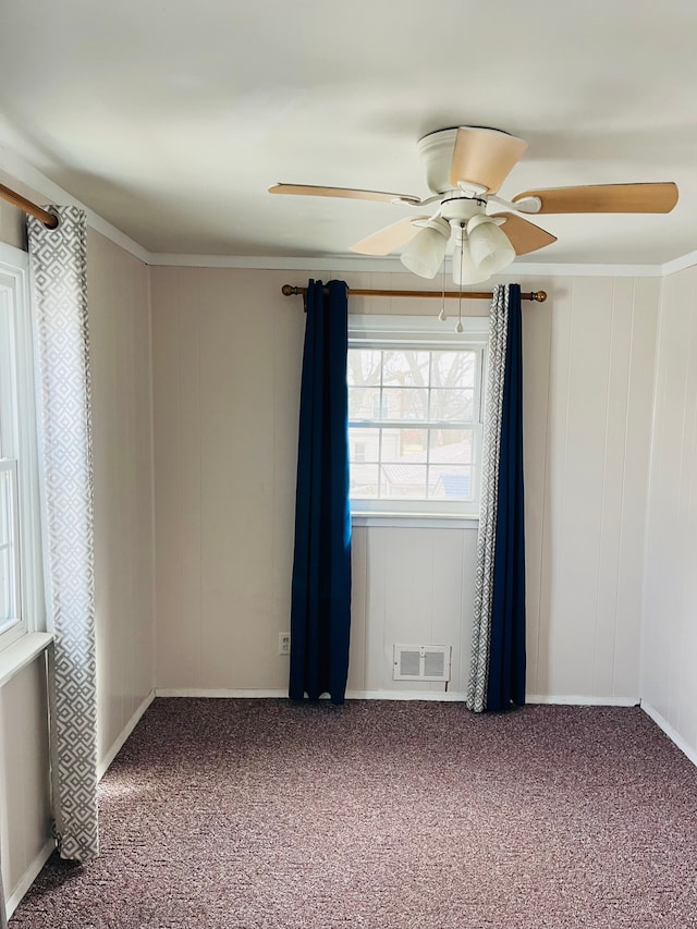 carpeted spare room with visible vents, ornamental molding, and a ceiling fan