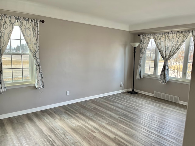 spare room featuring wood finished floors, visible vents, and baseboards