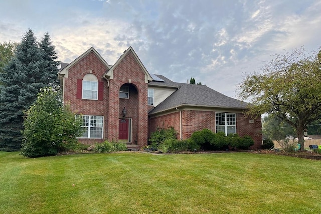 traditional-style home featuring brick siding, a front lawn, and roof with shingles