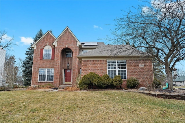 traditional-style home featuring solar panels, brick siding, roof with shingles, and a front yard