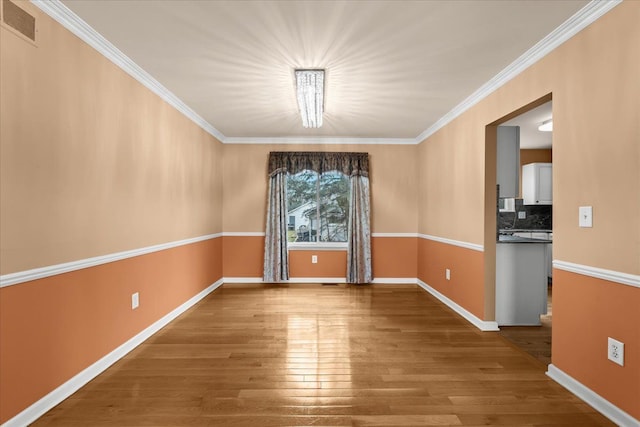 empty room featuring ornamental molding, wood finished floors, visible vents, and baseboards