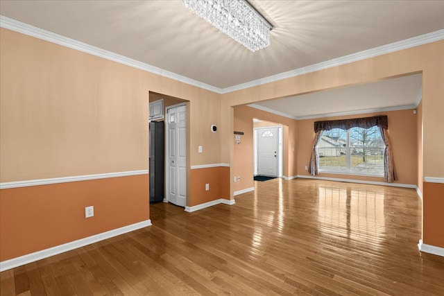 unfurnished living room featuring a chandelier, ornamental molding, wood-type flooring, and baseboards