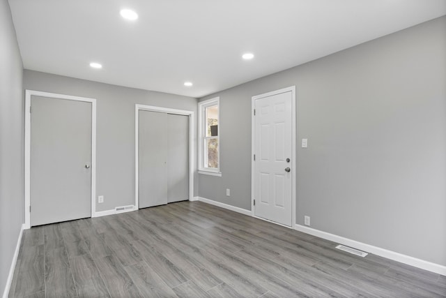 unfurnished bedroom featuring baseboards, visible vents, wood finished floors, two closets, and recessed lighting