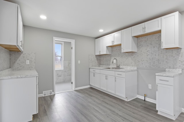 kitchen with tasteful backsplash, light wood-type flooring, visible vents, and a sink