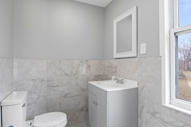 bathroom featuring a healthy amount of sunlight, toilet, tile walls, and vanity