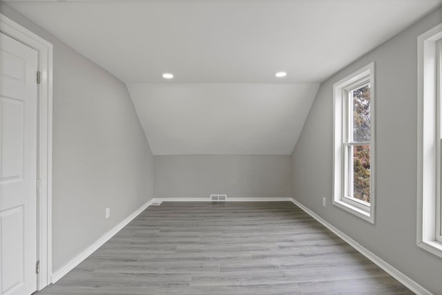 additional living space with visible vents, vaulted ceiling, light wood finished floors, and baseboards