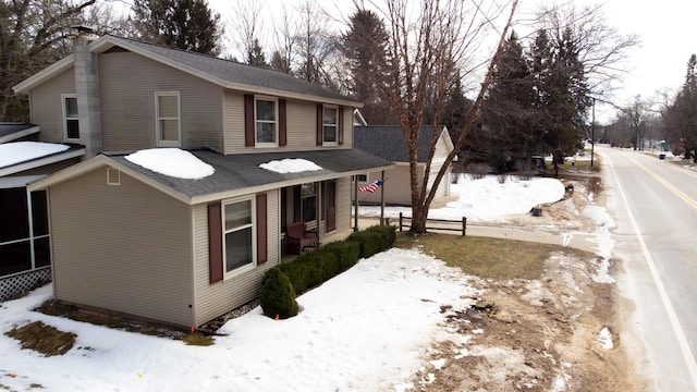 snow covered property with covered porch and a chimney