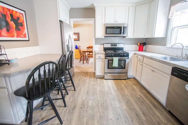 kitchen with stainless steel appliances, light countertops, light wood-type flooring, white cabinetry, and a sink