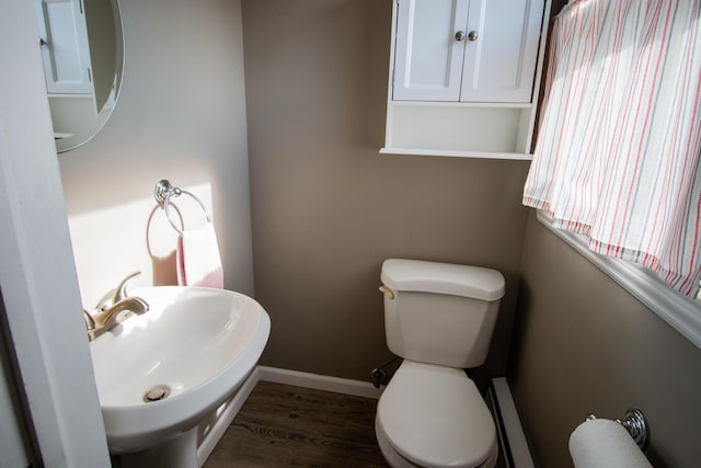 half bath with baseboards, a sink, toilet, and wood finished floors