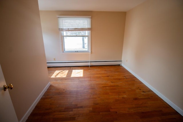 empty room with baseboards, a baseboard heating unit, and wood finished floors