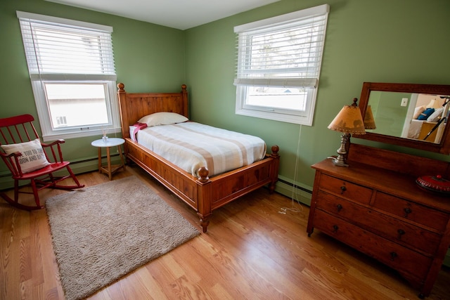 bedroom with multiple windows, a baseboard heating unit, and wood finished floors