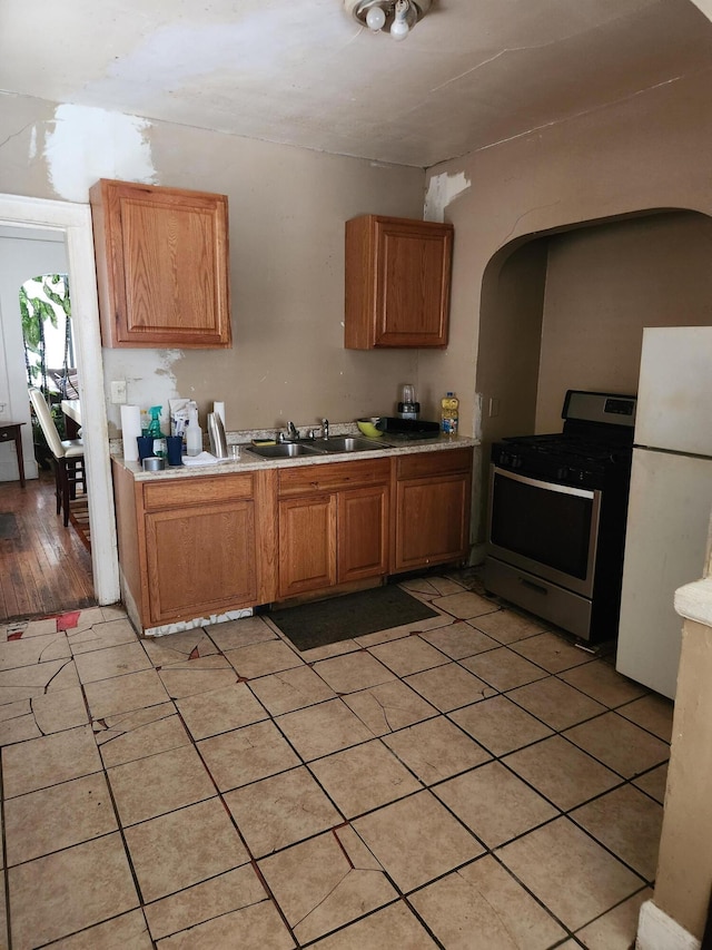 kitchen featuring brown cabinets, freestanding refrigerator, stainless steel gas range, light countertops, and a sink