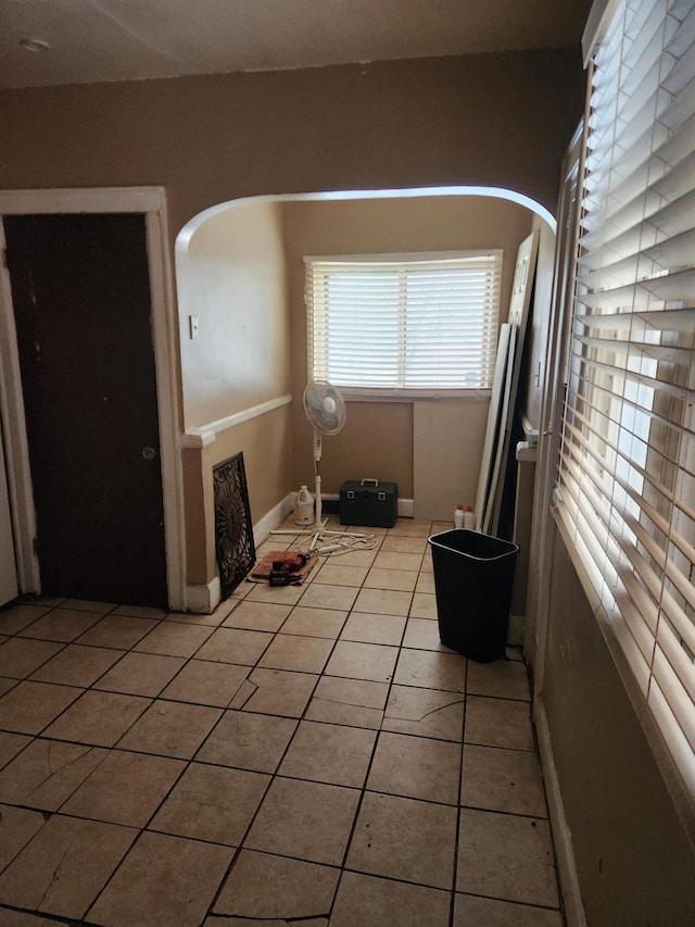 empty room with baseboards, arched walkways, and light tile patterned flooring