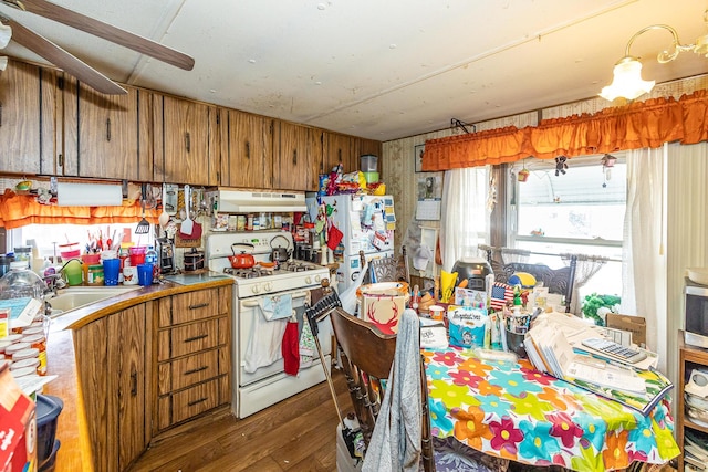 kitchen with brown cabinetry, a sink, white range with gas cooktop, and ventilation hood