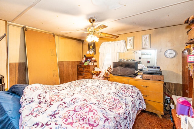 carpeted bedroom featuring a wainscoted wall, ceiling fan, and wooden walls