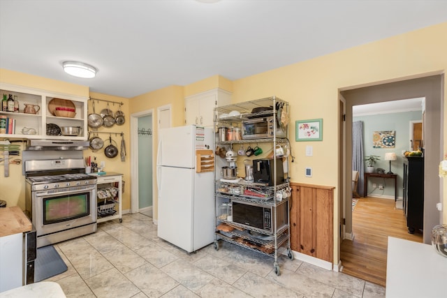 kitchen with a wainscoted wall, freestanding refrigerator, wood walls, gas range, and under cabinet range hood