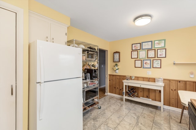 kitchen featuring wooden walls, white cabinets, a wainscoted wall, stainless steel microwave, and freestanding refrigerator