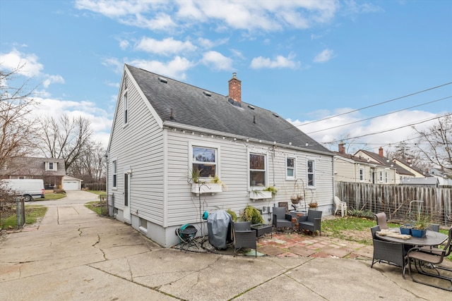 rear view of property with an outdoor structure, fence, roof with shingles, a chimney, and a patio area