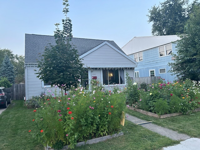 view of front of house with a garden, fence, a front lawn, and roof with shingles