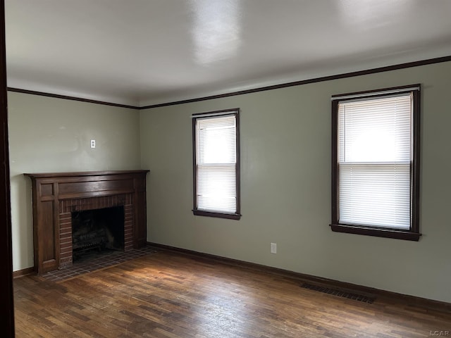 unfurnished living room with dark wood-style flooring, a fireplace, visible vents, ornamental molding, and baseboards