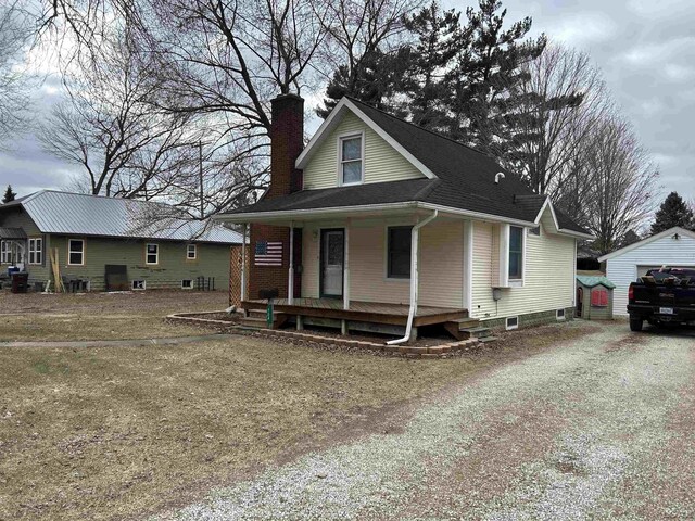 view of front facade featuring an outbuilding, a porch, a chimney, and gravel driveway