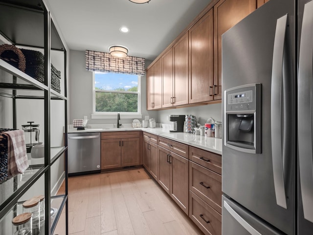 kitchen featuring a sink, light countertops, appliances with stainless steel finishes, light wood finished floors, and brown cabinetry