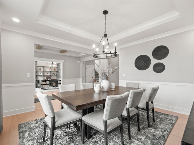 dining area featuring a raised ceiling, a wainscoted wall, an inviting chandelier, stairs, and light wood-type flooring