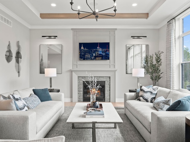 living area featuring a tray ceiling, a glass covered fireplace, visible vents, and an inviting chandelier