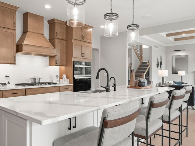 kitchen featuring tasteful backsplash, light wood-style flooring, custom exhaust hood, stainless steel appliances, and a sink