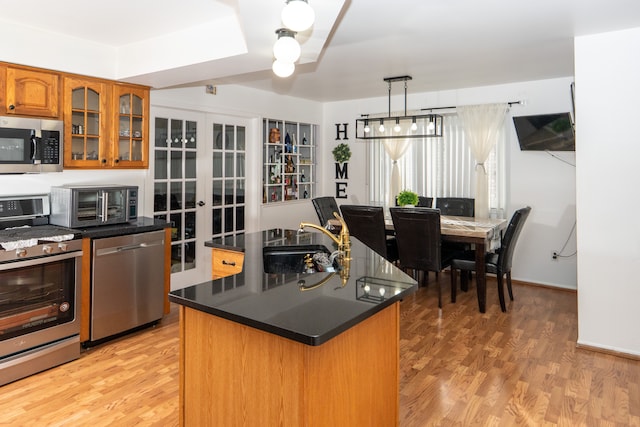 kitchen featuring stainless steel appliances, a kitchen island, light wood-style floors, brown cabinetry, and dark countertops