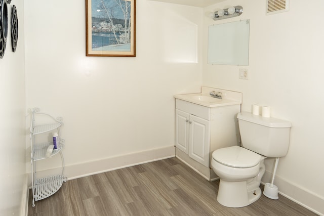 half bath featuring visible vents, toilet, vanity, wood finished floors, and baseboards