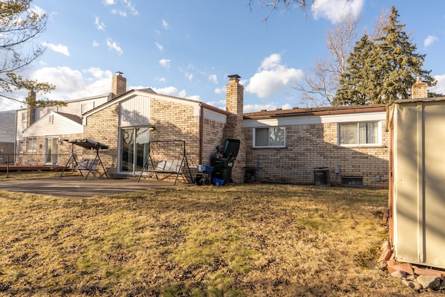 rear view of property with a patio, brick siding, fence, a lawn, and a chimney