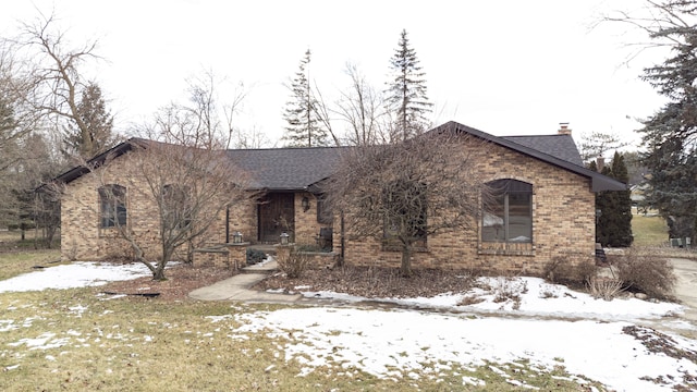 ranch-style home with a shingled roof, brick siding, and a chimney