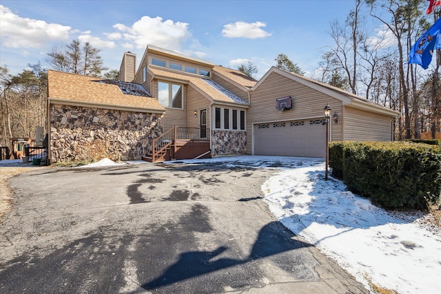 view of front facade featuring driveway, stone siding, an attached garage, and a chimney