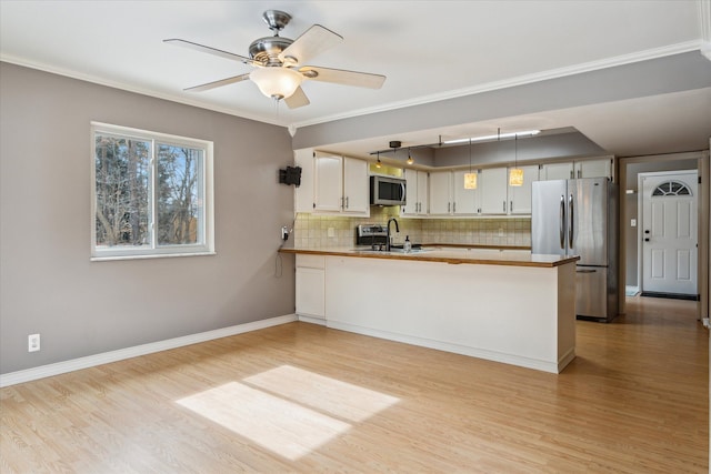 kitchen with crown molding, tasteful backsplash, light wood-style flooring, appliances with stainless steel finishes, and a peninsula